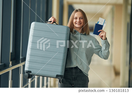 Excited, with tickets and luggage bag. Young woman in airport hall 130181813