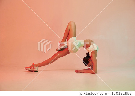 Head under the body, flexible. Young fitness woman in sportive clothes against background in studio Head under the body, flexible. Young fitness woman in sportive clothes against background in studio 130181992