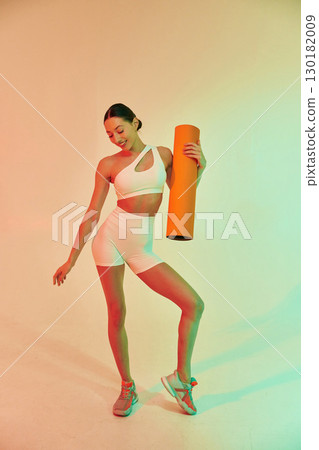 Happy person holding yoga mat. Young fitness woman in sportive clothes against background in studio 130182009
