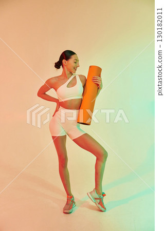 Happy person holding yoga mat. Young fitness woman in sportive clothes against background in studio 130182011