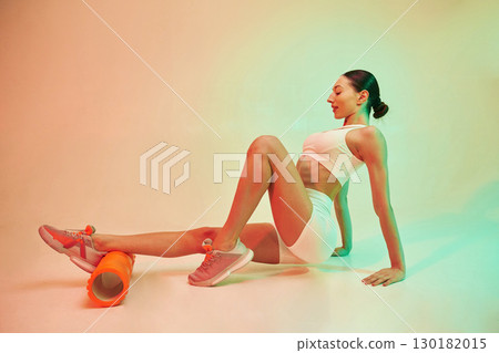 Using roller. Young fitness woman in sportive clothes against background in studio 130182015