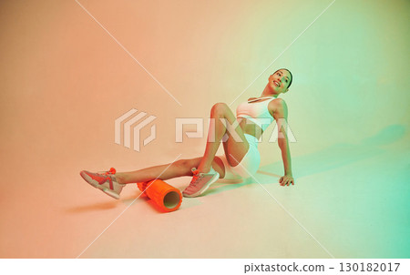 Using roller. Young fitness woman in sportive clothes against background in studio 130182017