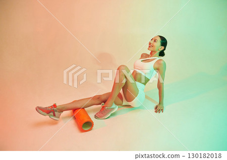With roller. Young fitness woman in sportive clothes against background in studio 130182018