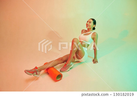 With roller. Young fitness woman in sportive clothes against background in studio 130182019