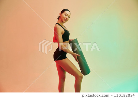 Time to practice, with yoga mat. Young fitness woman in sportive clothes against background in studio 130182054