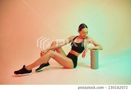 With roller. Young fitness woman in sportive clothes against background in studio 130182072