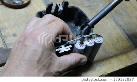 close-up of male hands with a small soldering iron welding contacts on old batteries from a construction tool, restoring battery life with DIY repairs 130182087