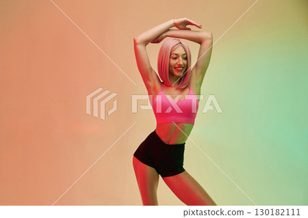 With hands up. Sportive woman with pink wig is against background With hands up. Sportive woman with pink wig is against background 130182111