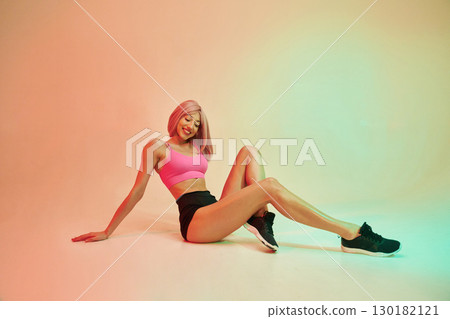 Sitting on the floor. Sportive woman with pink wig is against background Sitting on the floor. Sportive woman with pink wig is against background 130182121