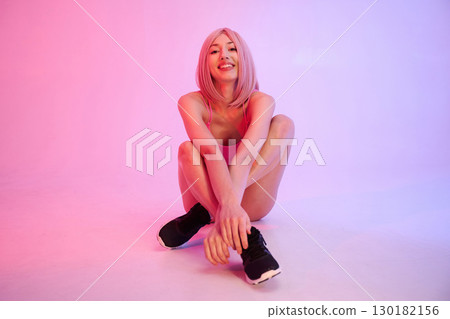Soft pink lighting. Sportive woman with wig is against background 130182156