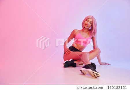 Taking a rest on the floor. Sportive woman with pink wig is against background 130182161