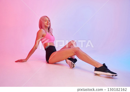 Taking a rest on the floor. Sportive woman with pink wig is against background Taking a rest on the floor. Sportive woman with pink wig is against background 130182162