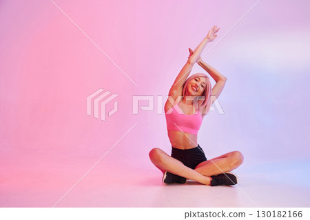 Practicing yoga. Sportive woman with pink wig is against background Practicing yoga. Sportive woman with pink wig is against background 130182166