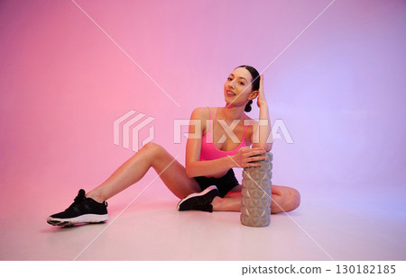 Wellbeing, with roller. Young fitness woman in sportive clothes against background in studio 130182185