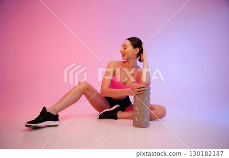 Wellbeing, with roller. Young fitness woman in sportive clothes against background in studio 130182187