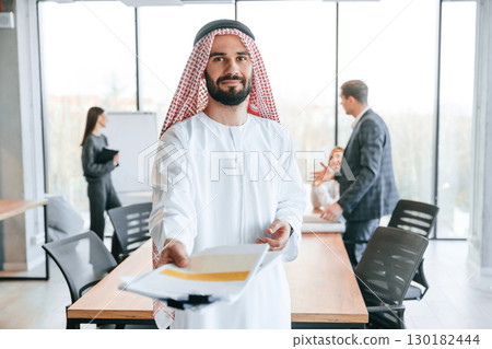 People behind Muslim businessman that is in traditional outfit with colleagues in office 130182444