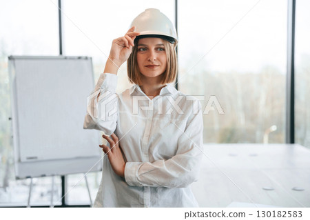 Young woman architect in hard hat is in office Young woman architect in hard hat is in office 130182583