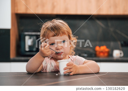 Portrait of cute little kid eating yogurt on the kitchen Portrait of cute little kid eating yogurt on the kitchen 130182620