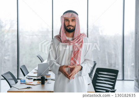 Against panoramic windows. Successful Muslim businessman in traditional outfit in his office 130182635