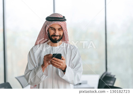 With smartphone in hand. Successful Muslim businessman in traditional outfit in his office 130182723