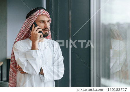 In the office with phone. Successful Muslim businessman in traditional outfit In the office with phone. Successful Muslim businessman in traditional outfit 130182727