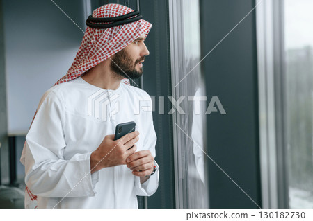 In the office with phone. Successful Muslim businessman in traditional outfit 130182730