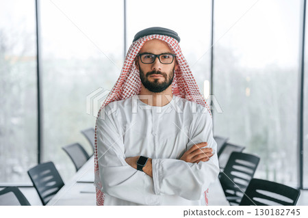 Young investor is standing. Successful Muslim businessman in traditional outfit in his office Young investor is standing. Successful Muslim businessman in traditional outfit in his office 130182745