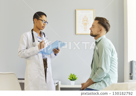 Clinic room meeting, female doctor talking, asking male patient sitting on examination bed Clinic room meeting, female doctor talking, asking male patient sitting on examination bed 130182792