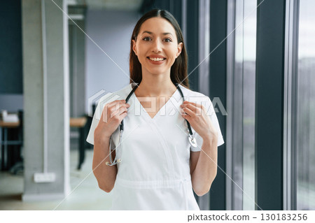 Standing and posing. Female doctor in white coat is indoors 130183256
