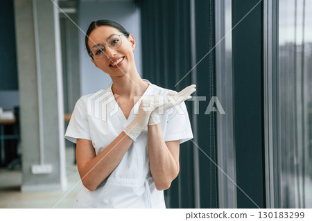 Cheerful female doctor in white coat is indoors standing and smiling 130183299