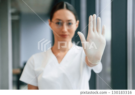 Stop sign by hand. Female doctor in white coat is indoors 130183316
