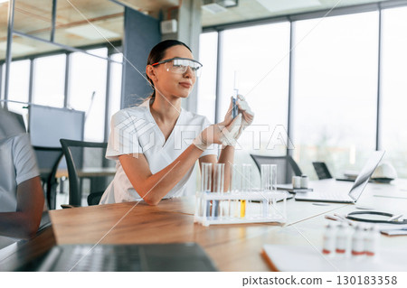 Working with bunch of test tubes. Female doctor in white coat is indoors Working with bunch of test tubes. Female doctor in white coat is indoors 130183358