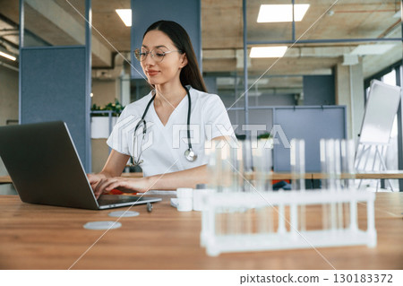 Empty test tubes on the table. Female doctor in white coat is indoors Empty test tubes on the table. Female doctor in white coat is indoors 130183372