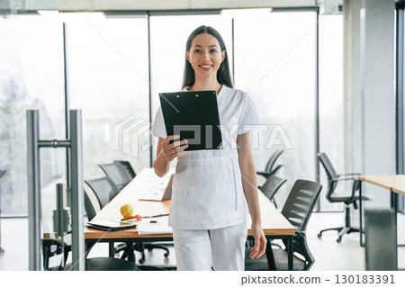Black notepad in hands. Female doctor in white coat is indoors 130183391