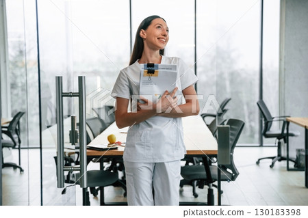 Near glass door. With documents. Female doctor in white coat is indoors 130183398