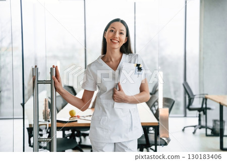 Leaving the meeting room. Standing with documents. Female doctor in white coat is indoors 130183406
