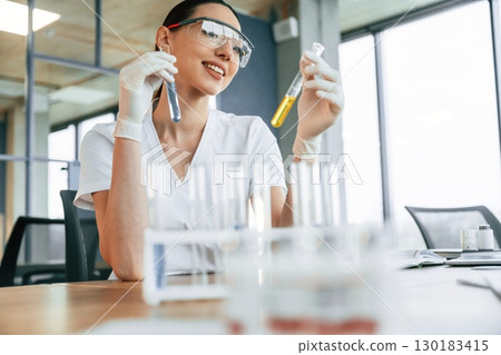 Doing research by using chemicals in test tubes. Female doctor in white coat is indoors 130183415