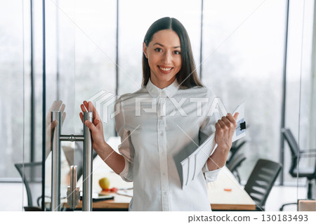 Standing and holding documents in hands. Businesswoman is indoors in the office Standing and holding documents in hands. Businesswoman is indoors in the office 130183493