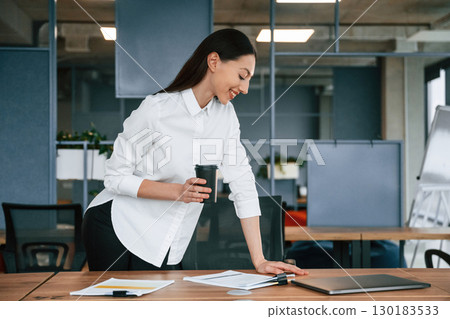 Holding drink in hand. Businesswoman is indoors in the office 130183533