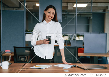Holding drink in hand. Businesswoman is indoors in the office 130183534