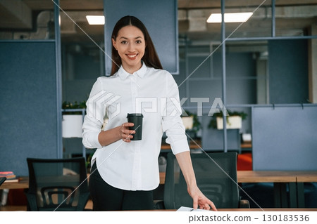 Holding drink in hand. Businesswoman is indoors in the office 130183536