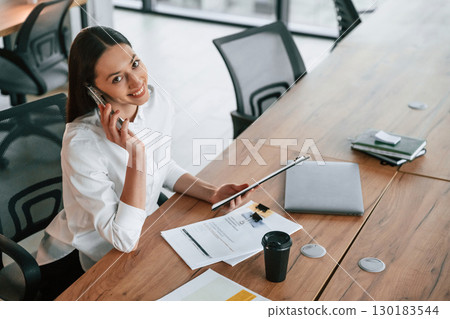 Talking by phone. Businesswoman is indoors in the office Talking by phone. Businesswoman is indoors in the office 130183544