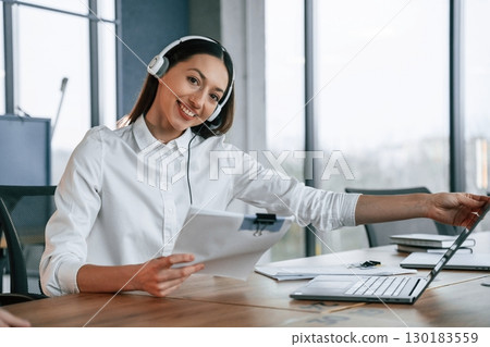 Technical support. In headphones. Businesswoman is indoors in the office Technical support. In headphones. Businesswoman is indoors in the office 130183559