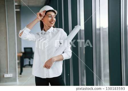 Female architect in hard hat and in white clothes is indoors Female architect in hard hat and in white clothes is indoors 130183593