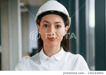 Portrait of female architect that is in hard hat and in white clothes indoors Portrait of female architect that is in hard hat and in white clothes indoors 130183603