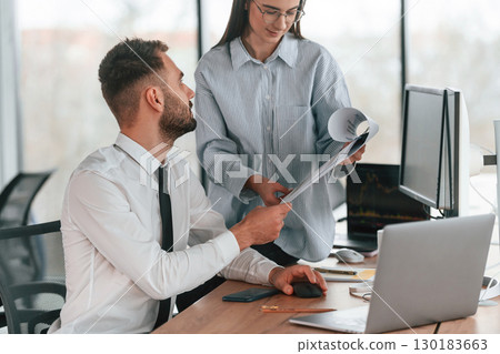 Silver colored laptop is on the table. Two employees are working in the office together Silver colored laptop is on the table. Two employees are working in the office together 130183663