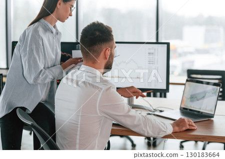 Brokers with monitors with graphs on the table. Two employees are working in the office together Brokers with monitors with graphs on the table. Two employees are working in the office together 130183664