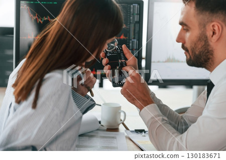 Brokers with monitors with graphs on the table. Two employees are working in the office together 130183671