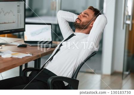 Taking a break, resting. Businessman is sitting by computer and working in the office Taking a break, resting. Businessman is sitting by computer and working in the office 130183730