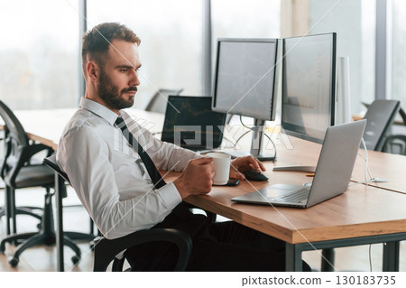 Using laptop. Businessman is sitting by computer and working in the office Using laptop. Businessman is sitting by computer and working in the office 130183735